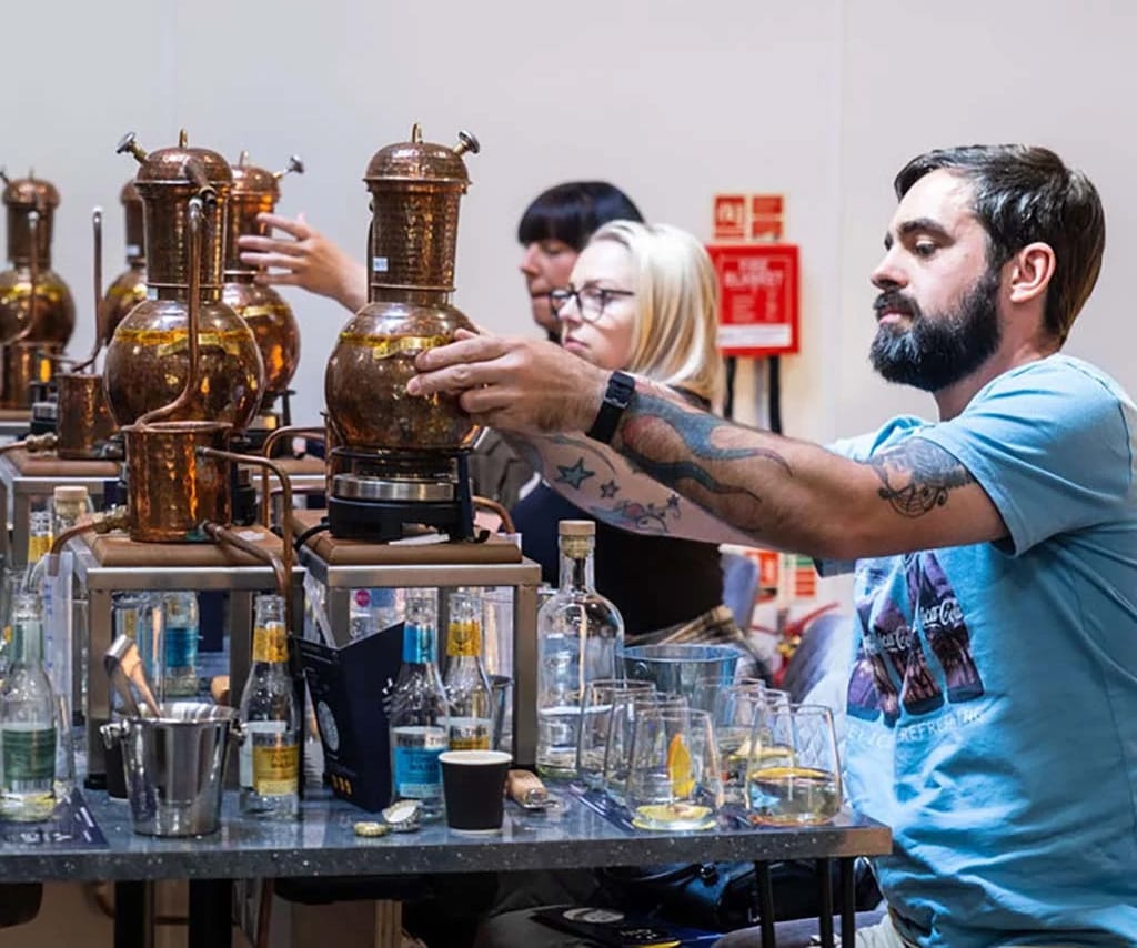 People attending a gin-making class using copper stills at a distillery, with drinks and ingredients on the tables.